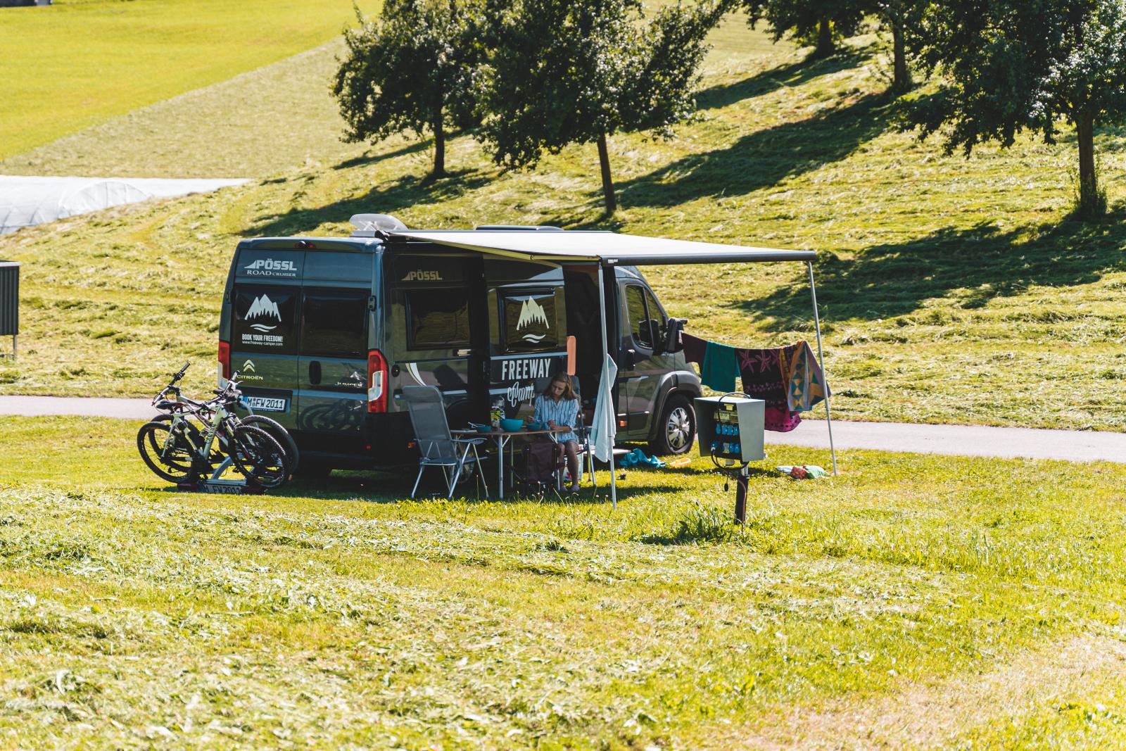 Frau sitzt gemütlich vor Campervan mit Fahrrädern