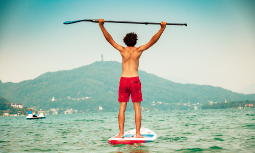 © Fotograf / Tourismus Region Klagenfurt / Freiluft-Fitnesscenter mit Traumaussicht: Beim Stand-up-Paddeln hat schon das Stehen am Board einen Trainingseffekt. Aktiv am See in Kärnten: mit Board und Yogamatte