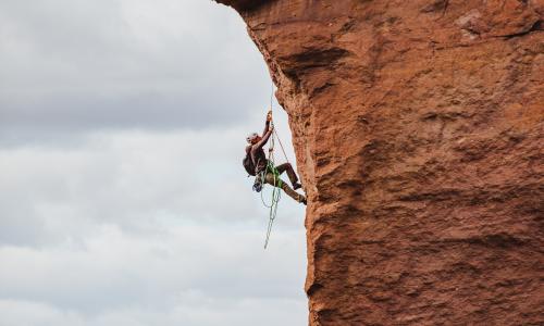 Mann klettert in voller Ausrüstung eine rotbraune Felsenwand hoch.