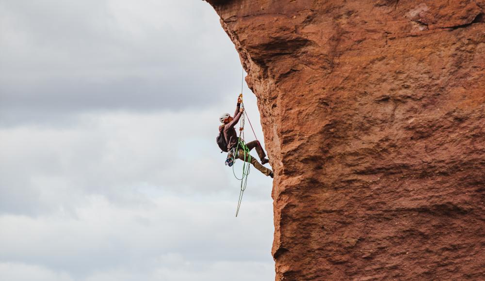 Mann klettert in voller Ausrüstung eine rotbraune Felsenwand hoch.